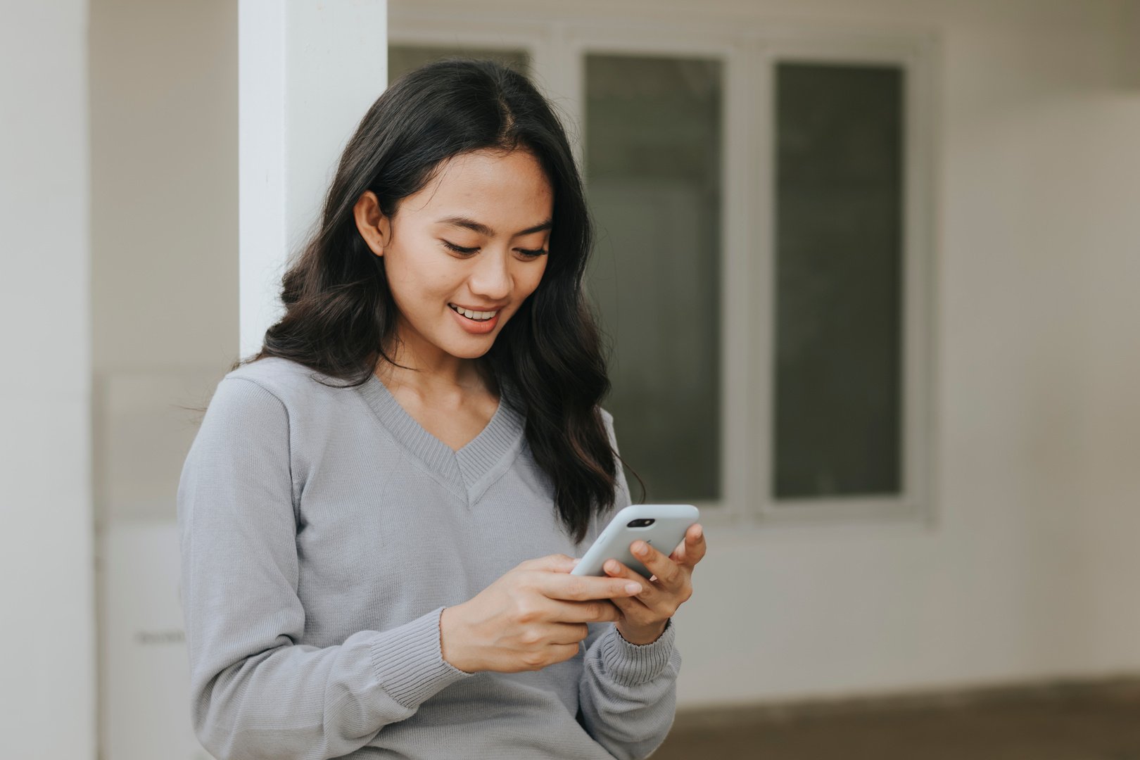 Woman Smiling While Looking Down Her Phone